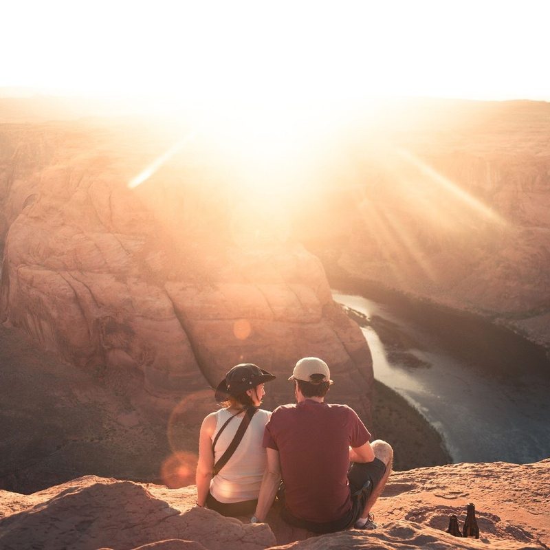 A hiking couple sit and watch the sunset over rocky outcrops