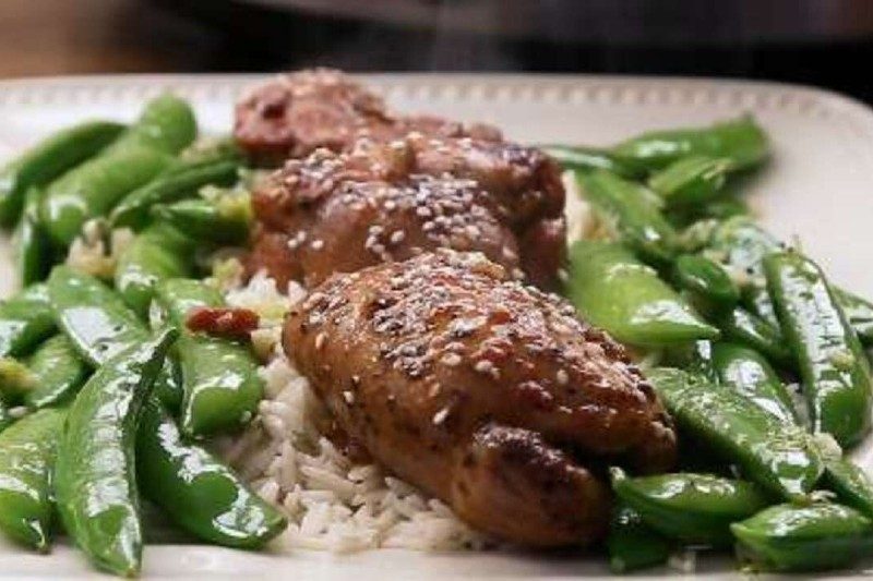 honey garlic chicken thighs on a plate with snap peas and rice.