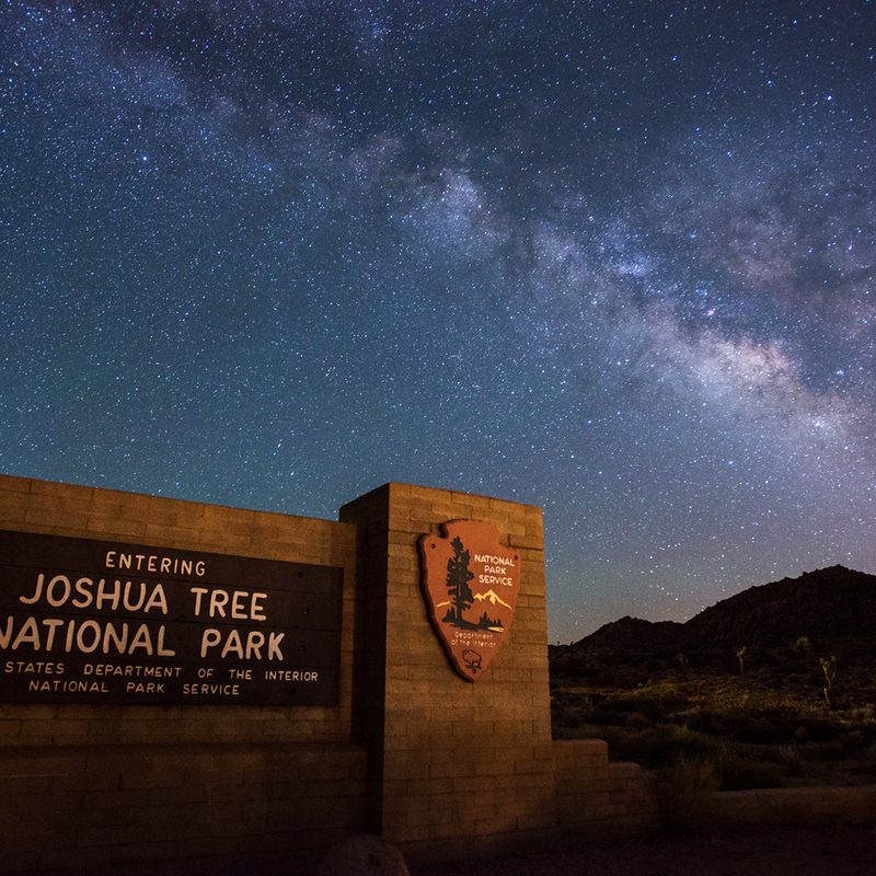 A sign that says "Joshua Tree National Park" at night.