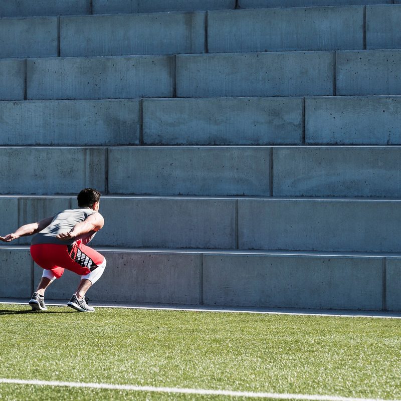 Athlete doing jump squats in front of a field stairway.