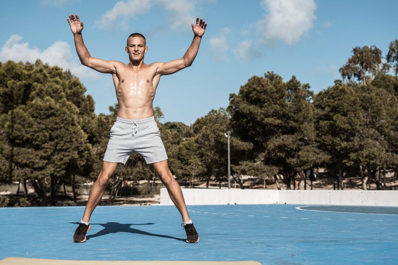 Shirtless man doing jumping jacks.