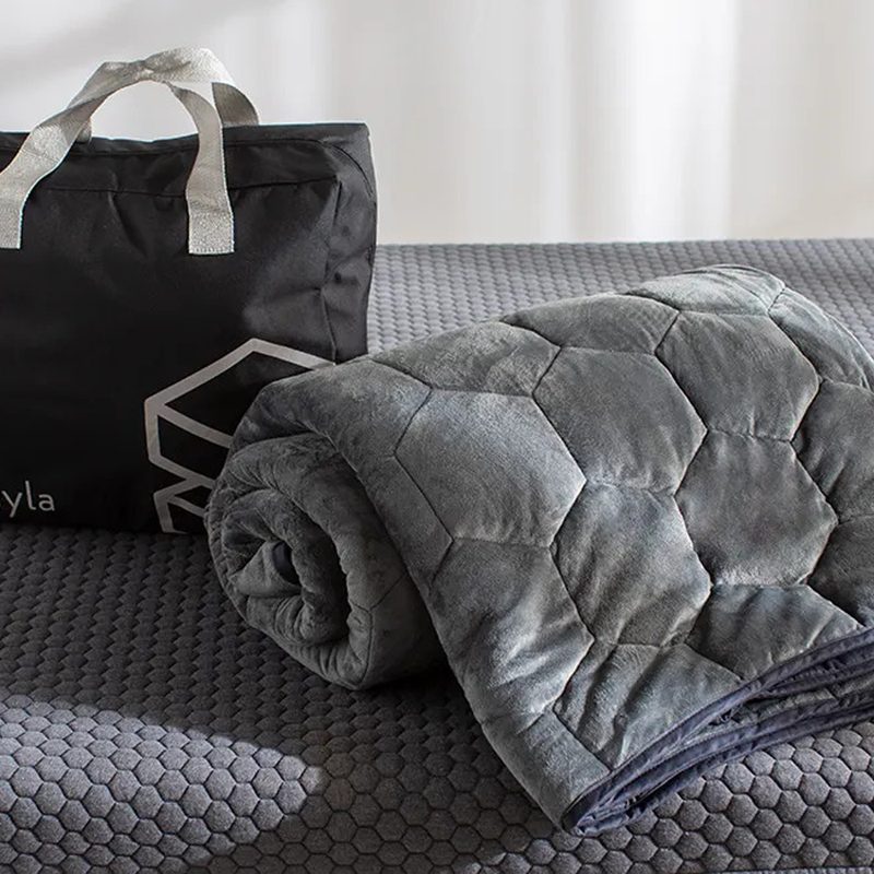 A rolled up Layla Weighted Blanket and a Layla bag on top of a bed.