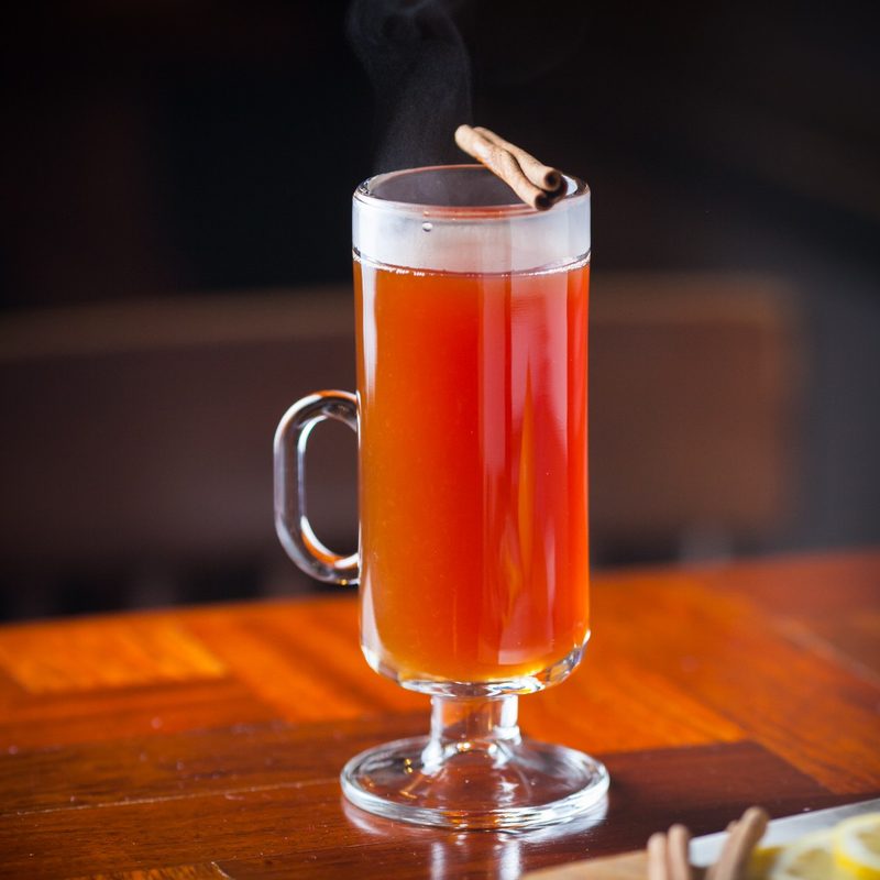 hot cup of Noilly Toddy garnished with a cinnamon stick sitting on a table.
