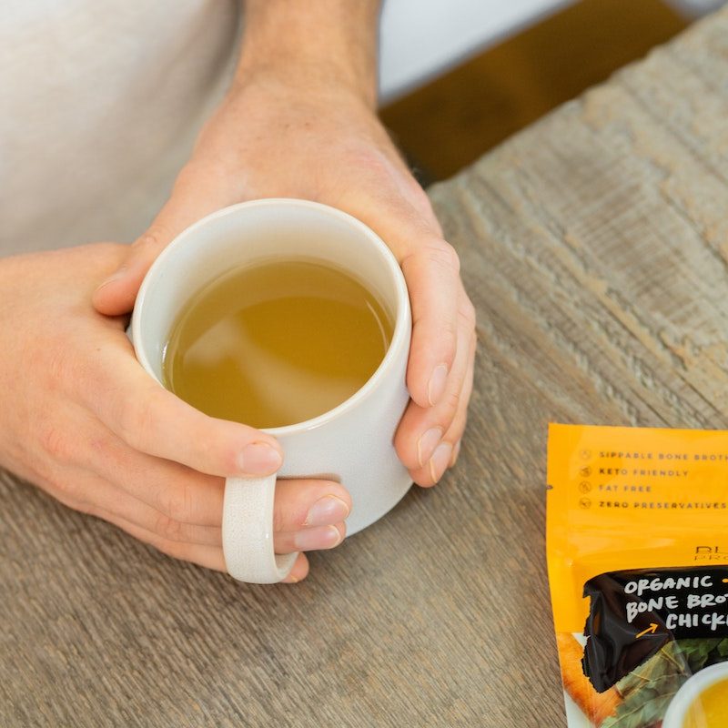person holding a mug of hot bone broth in their hands.