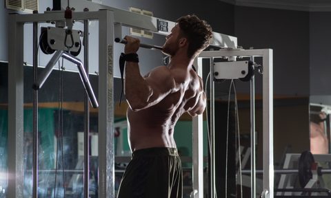Man doing pull-ups on silver bar in gym shirtless wearing gloves