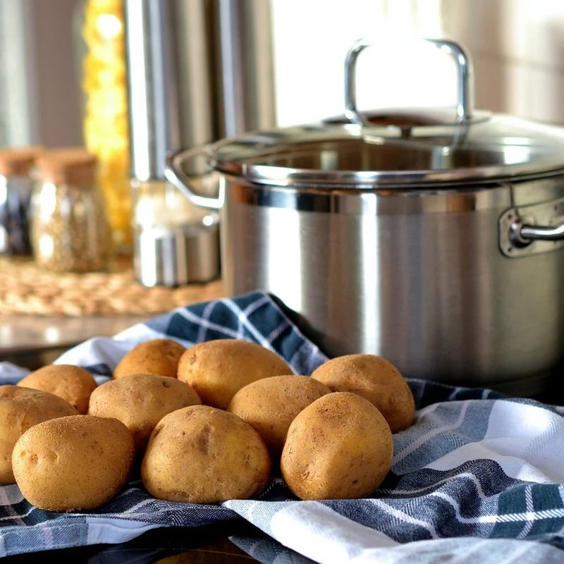 Potatoes on blue cloth and a stainless steel pot on a kitchen table.