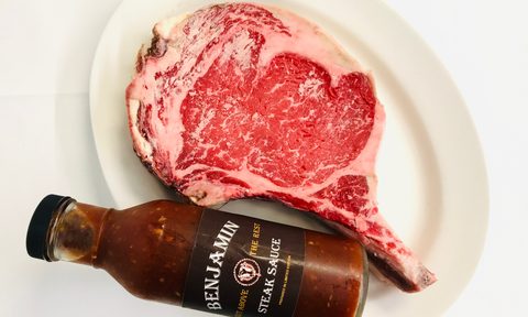 Raw ribeye with Benjamins Steak Sauce on a plate.