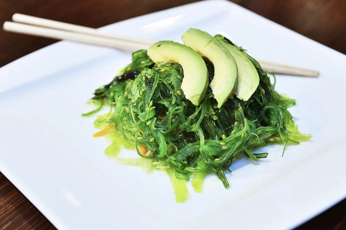 seaweed salad wakame with avocado on white square plate with chopsticks