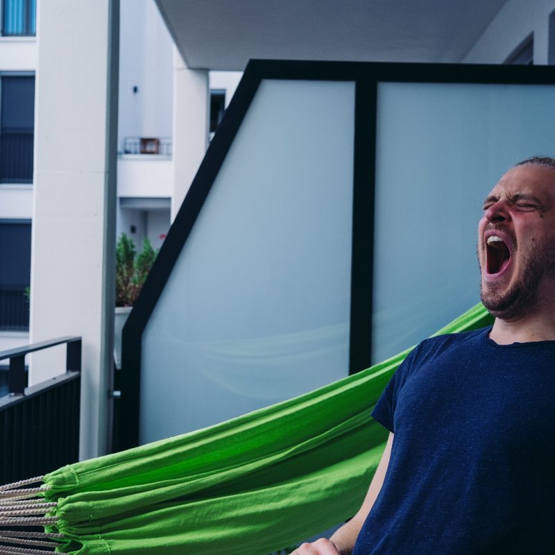 Man sitting on a balcony while he is yawning.