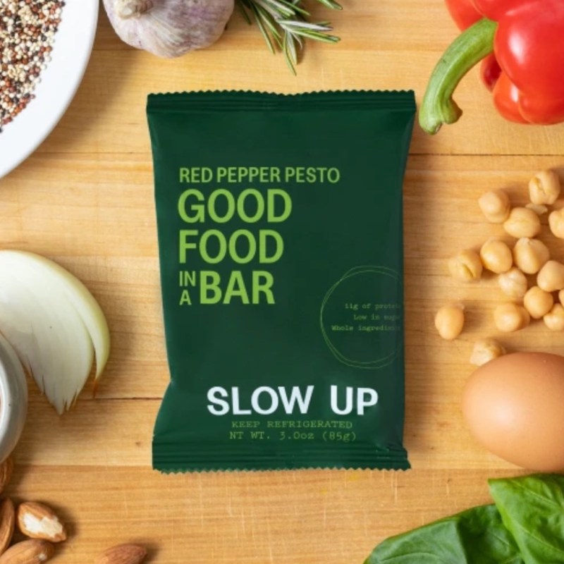slow up bar sitting on a counter with nuts, vegetables, and seeds.