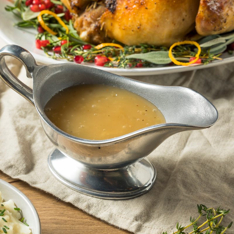 A giblet gravy in a gravy boat on a table cloth, surrounded by various dishes