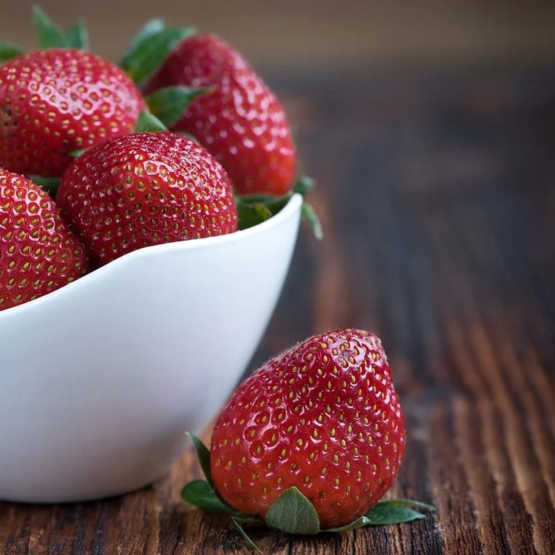 close up of strawberries in a white bowl sitting on a counter.