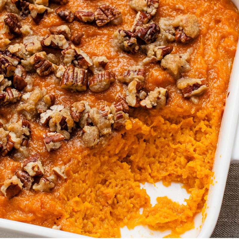 Sweet potato casserole topped with pecans in a white casserole dish.