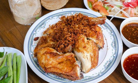 Thai Gai Yang grilled chicken on a plate with som tum salad in the background.