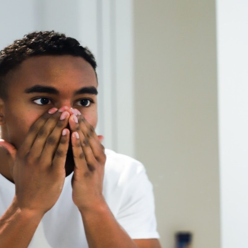Man looking at his face in the mirror with his hands over his nose and mouth