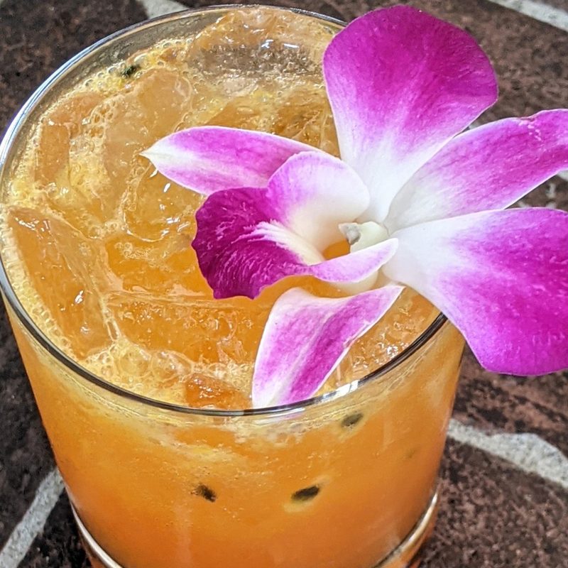 A closeup of a glass of Passion Project cocktail with orchid flower on a table.