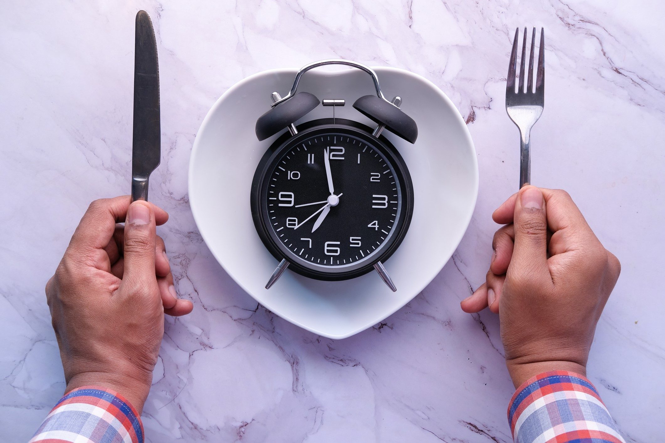 Man holding spoon and fork in between a clock placed on a plate