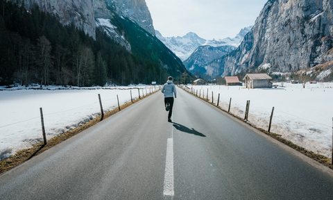 Man running on a cold day on a road running through the mountains
