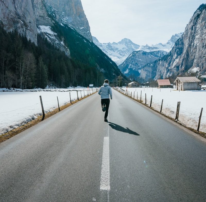 Man running on a cold day on a road running through the mountains.