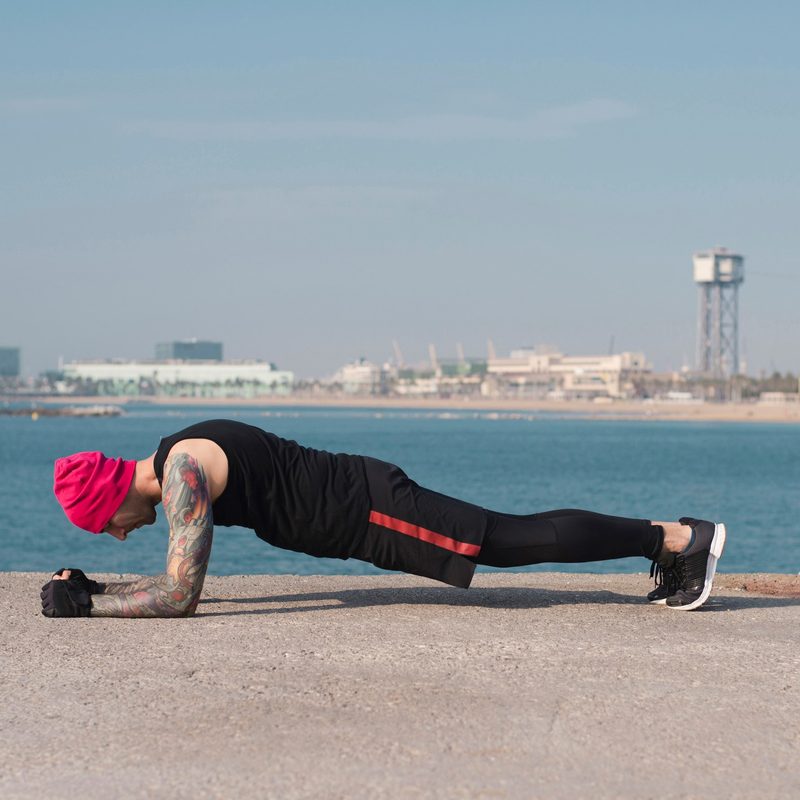 Side view of a man doing up-down planks at a beach.
