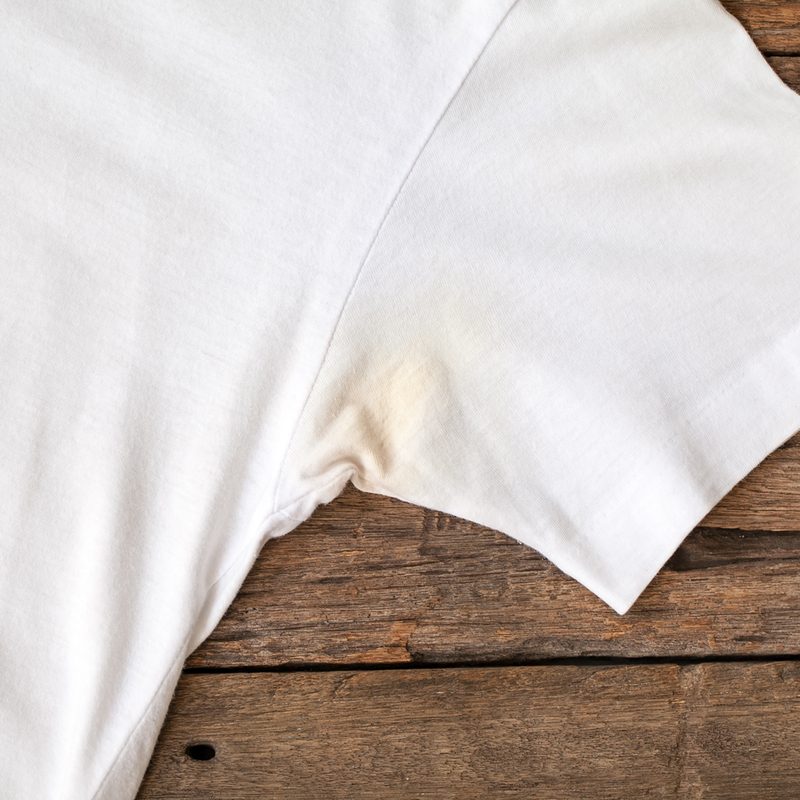 A deodorant stain on a white shirt on a wooden surface.