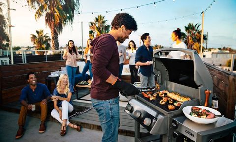 Young man grilling on patio with friends during a party.