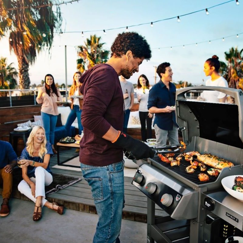 Young man grilling on patio with friends during a party.