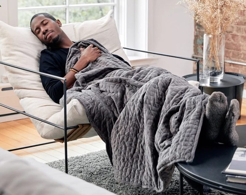 A man sleeping on a chair with a weighted blanket in a room.
