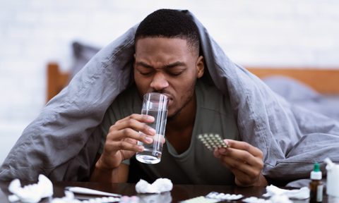Sick man taking pills and drinking water and lying In bedroom.
