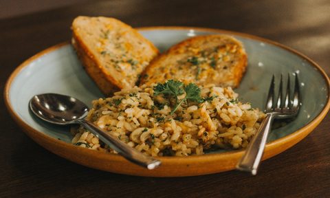 A brown rice-based dish with toasted bread slices served on a plate with spoon and fork.