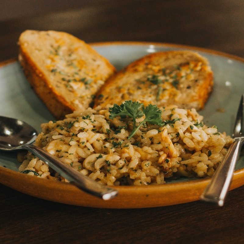 A brown rice-based dish with toasted bread slices served on a plate with spoon and fork.