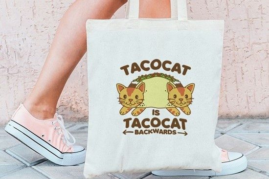 TacoCat tote bag displayed near a person's feet.