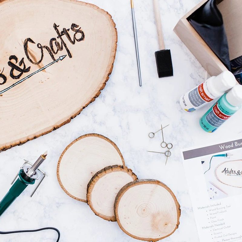 A tree stump with the words "Adults & Crafts" along with three smaller tree stumps, an instruction sheet, and a box filled with craft supplies.
