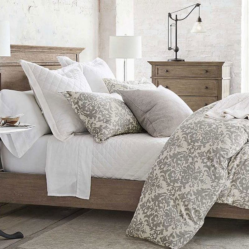 A wooden bed with pillows and a comforter near a bedside table with potted plant and decor in a bedroom.