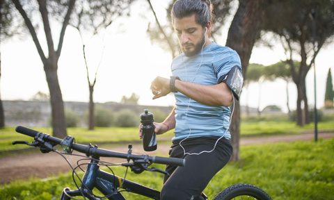 A male cyclist with water bottle checking his watch in a park on a sunny day.