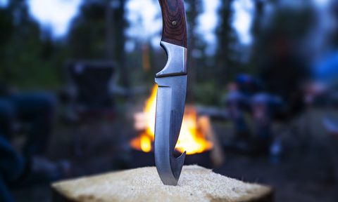 Closeup of hunting fishing camping knife blade In campfire log In outdoor scene