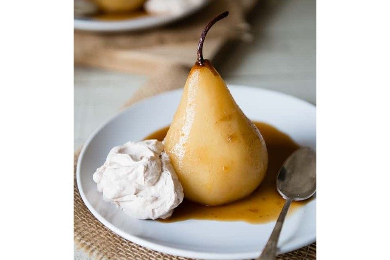 chai poached pear with whipped cream sitting on a plate.