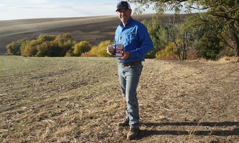 Farmer Nathan in the field holding a bottle of Copperworks Distilling's single malt, salmon-safe whiskey.