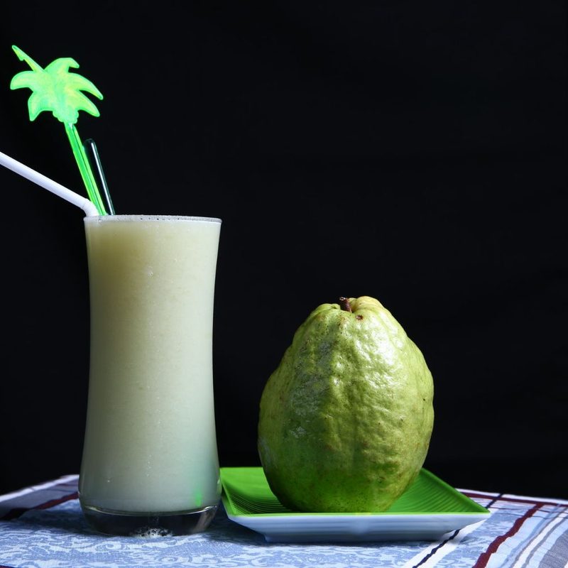 Guava fruit sitting next to a guava drink