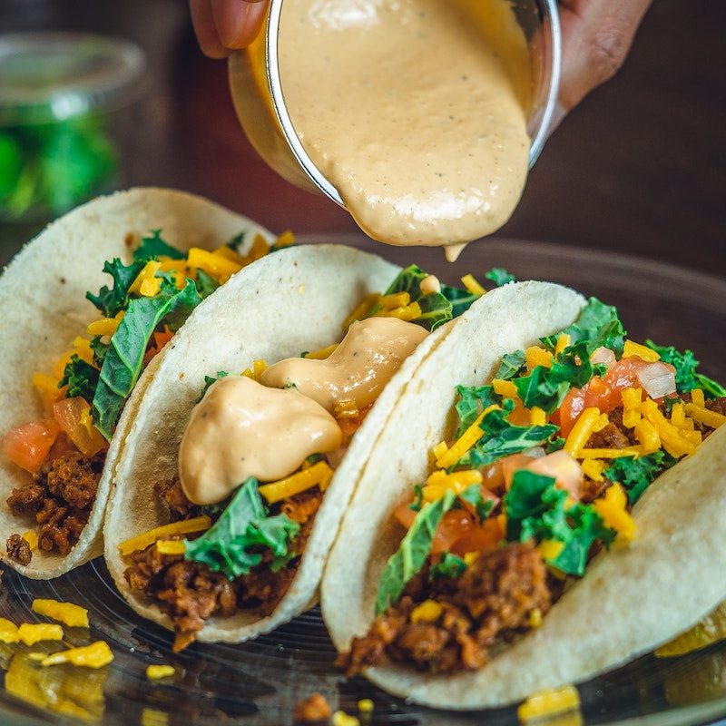 Person pouring sauce on veggie tacos.