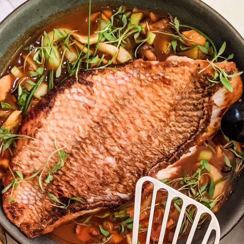 fish cooking in a pot with vegetables.