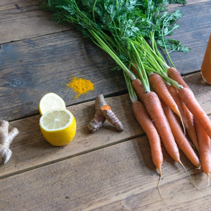 Ginger root, lemon, turmeric, carrots, and a detox drink sitting on a counter
