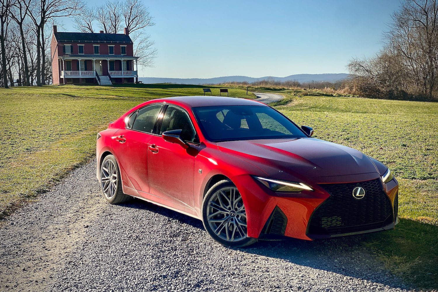 Lexus IS 500 front end from passenger's side with a house and gravel road in the back.