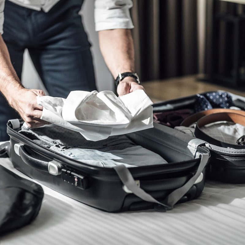 A person packing their suitcase with dress clothing.