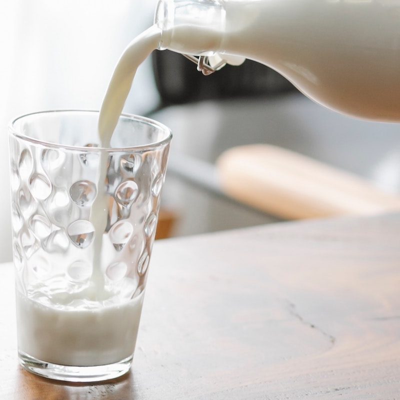 Person pouring a glass of milk.