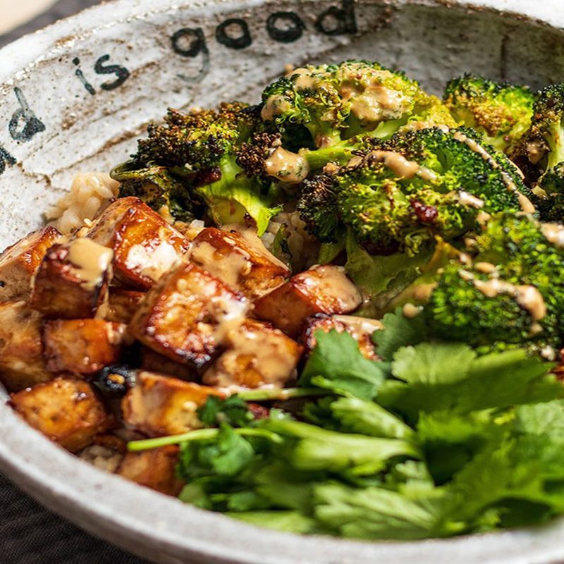 A close-up of a bowl of miso-roasted broccoli and tofu Buddha bowl with sesame dressing.