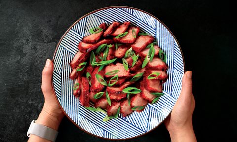 Hands holding a plate of Nom Nom Char Siu, black table in the back.