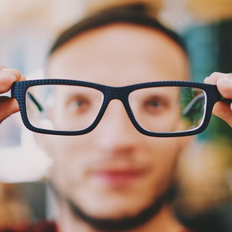 Man holding up glasses; blurred vision