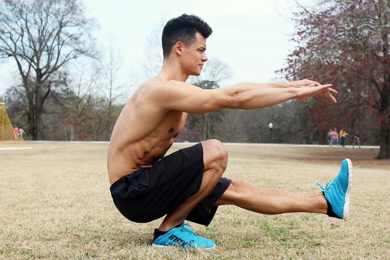 Man doing pistol squat black shorts blue sneakers outside tree