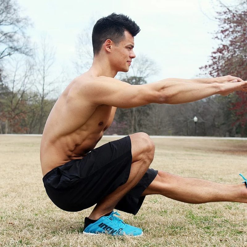 A man doing pistol squat in an open field.